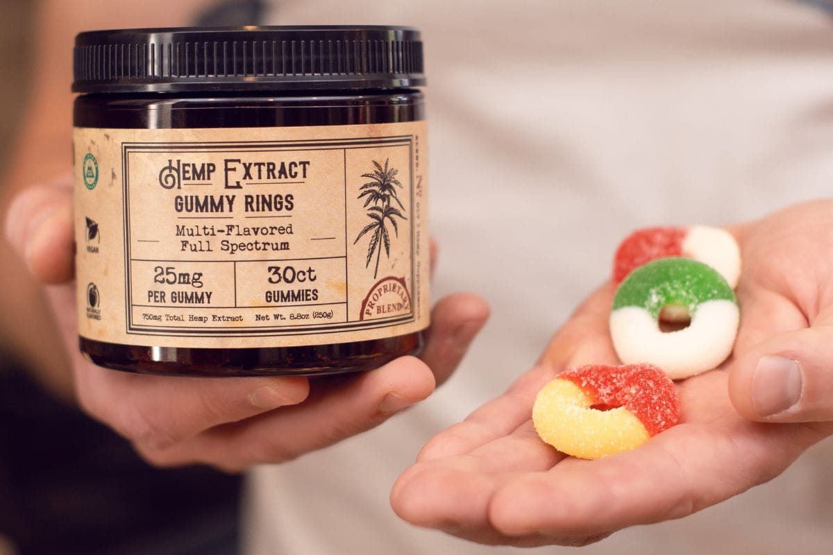 A person holding jar of cbd gummies and some gummies in his left hand